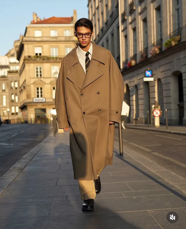 Fashion reel still: a man in a long camel coat walking a city street.